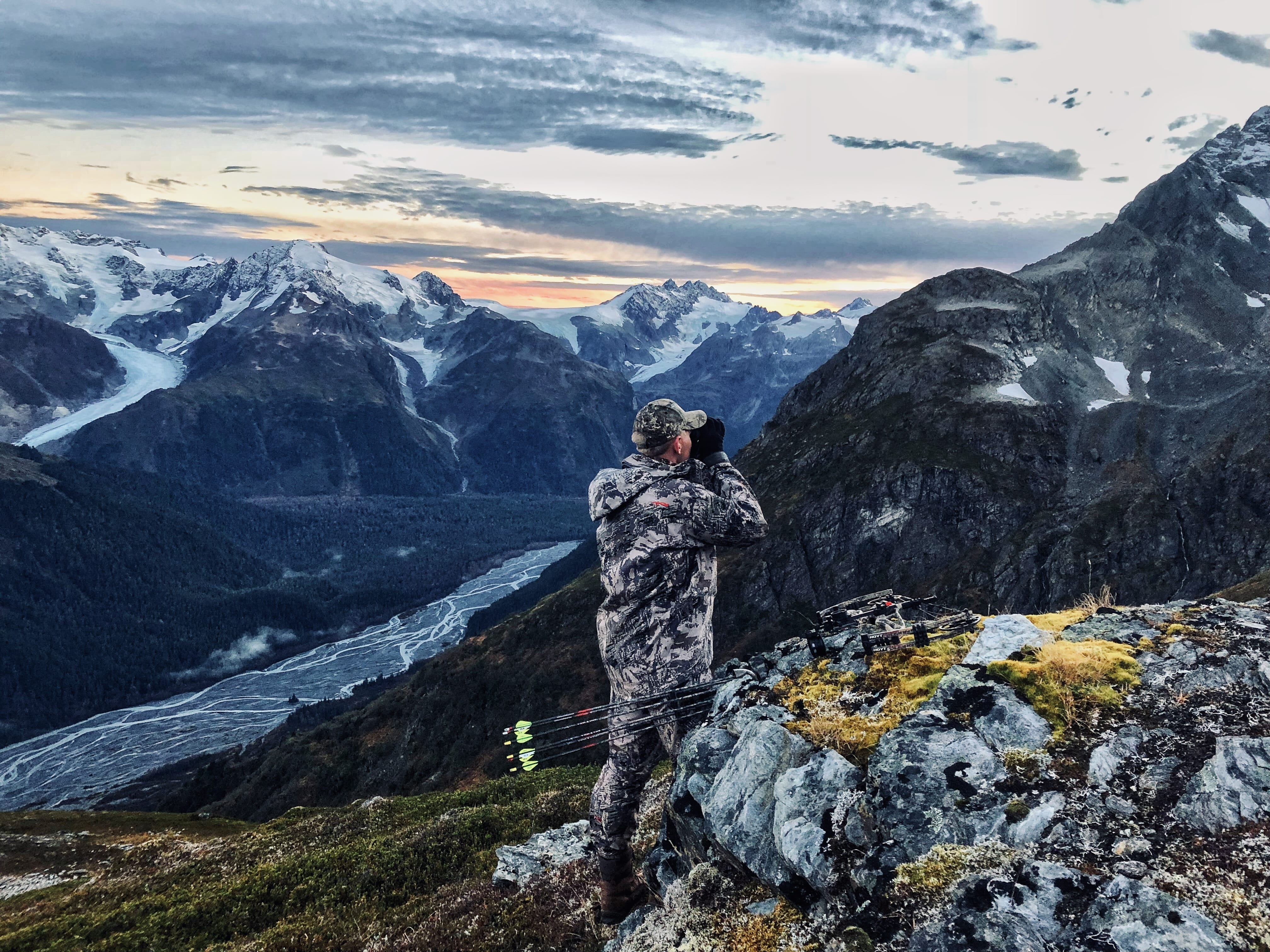 A bowhunter glassing snow capped peaks for mountain goats.